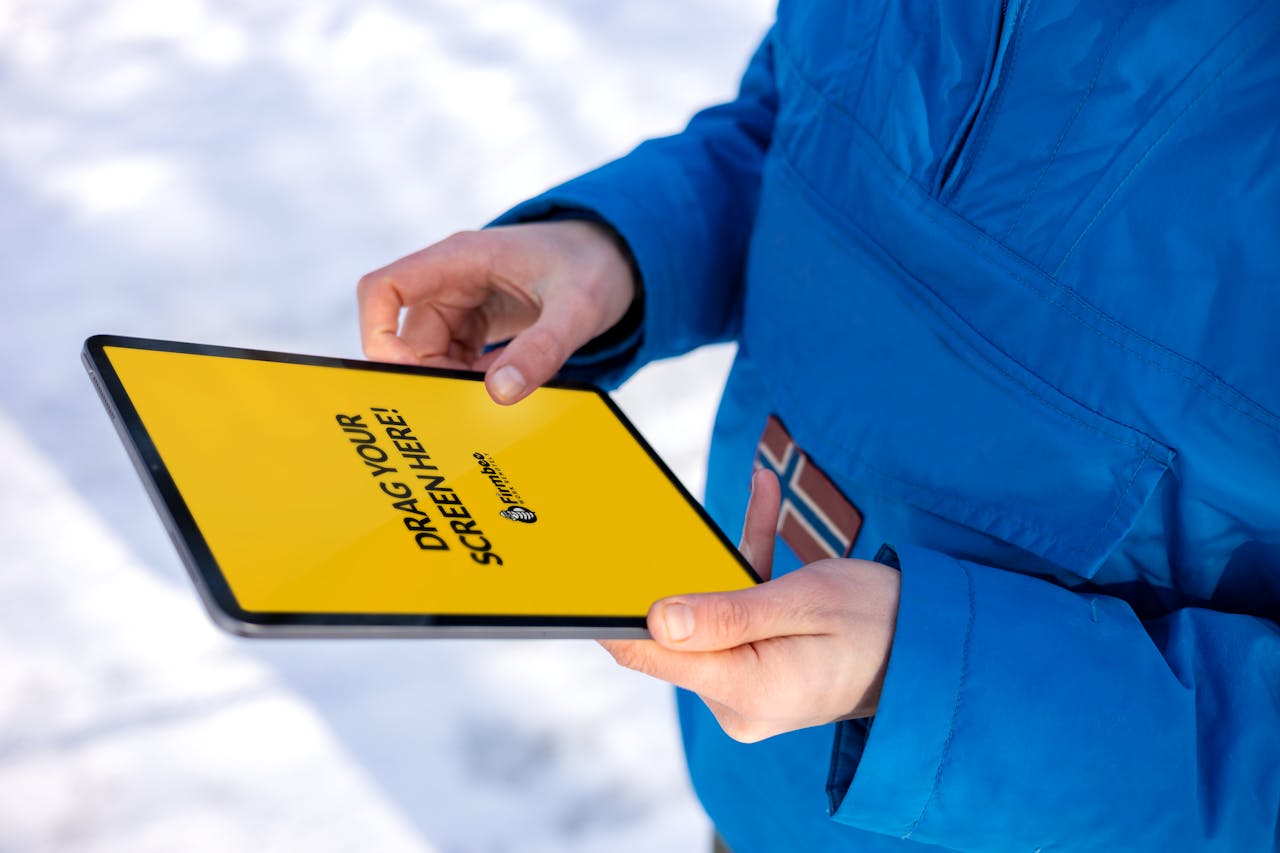 Close-up of hands holding a tablet with a yellow screen in a snowy outdoor setting.